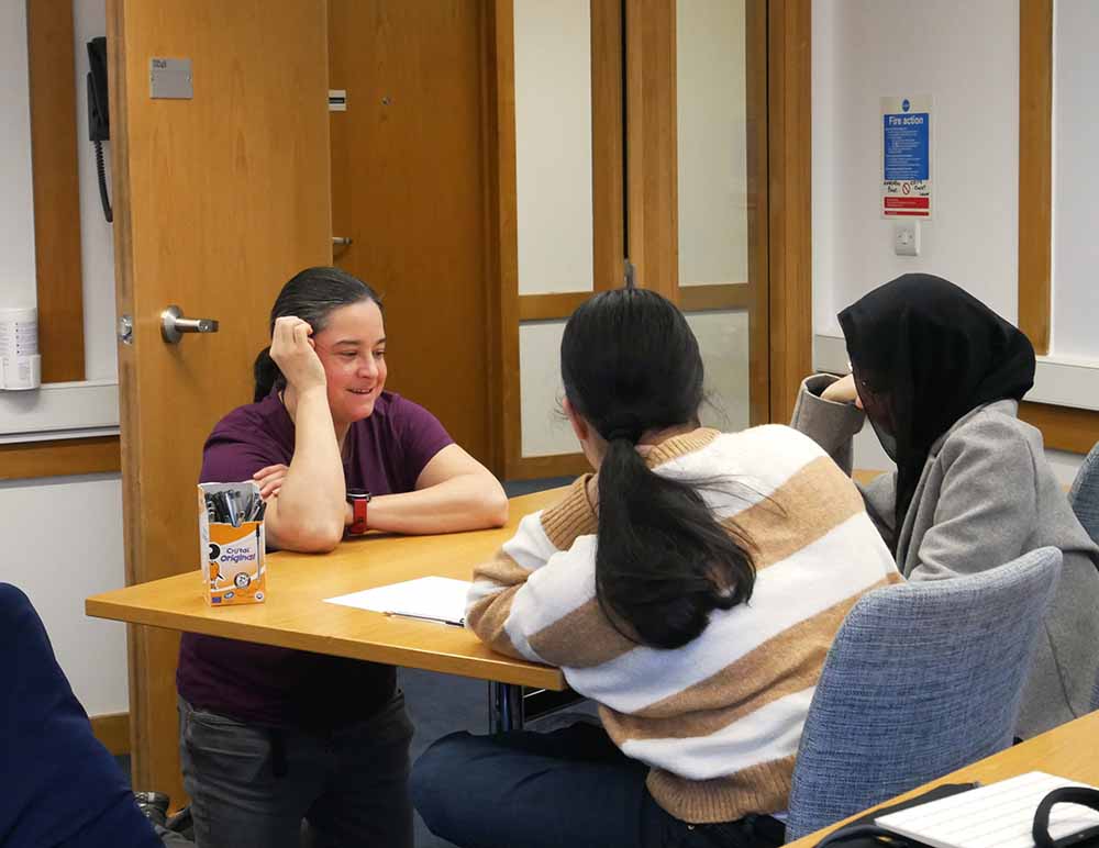 two students sitting at a table with a mentor, working on a problem.