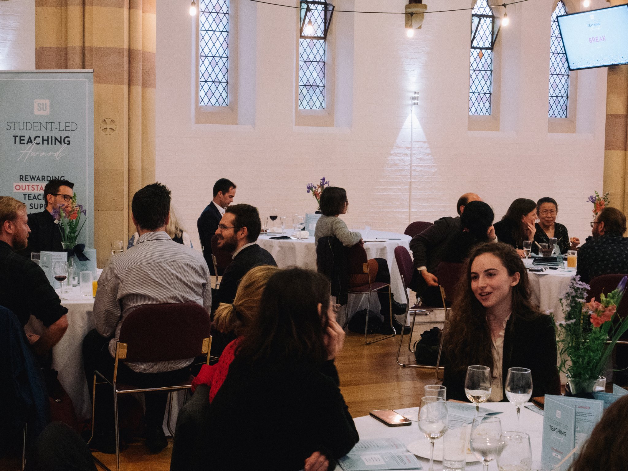 People are sat around circular tables talking, there is an SLTA banner in the background of the photo